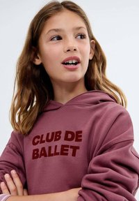 Bordo mikina s velkým grafickým nápisem "CLUB DE BALLET" v tmavě červené barvě. Obsahuje přední kapsu a měkký materiál, s volným střihem.