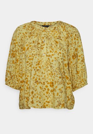 Blusa floral em tecido amarelo claro, com flores laranjas. Mangas bufantes, decote redondo e detalhe de botão na frente. Textura suave e leve.