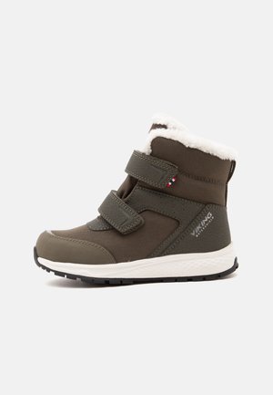 Bota infantil marrón impermeable de invierno con forro blanco de forro polar y dos tiras ajustables de velcro, mostrada de lado.