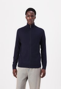 Navy zip-up sweater in a soft knit fabric with a high collar and ribbed hem, paired with light denim pants.