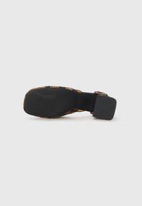 Flat shoe with a black rubber sole, embellished with gold and black beaded detailing on the upper, featuring a wide, square heel.