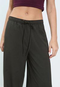 Donkergroene broek met een losse pasvorm, gemaakt van lichtgewicht stof, voorzien van een elastische tailleband met trekkoord en zijzakken.