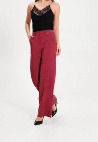 Breda burgundisk färgade byxor med en slät textur, i kombination med en svart topp med spetsdetaljer. Outfiten kännetecknas av rena linjer och minimala detaljer.