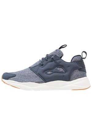 Zapatilla deportiva gris y negra con parte superior de tela, cierre de cordones, pestañas para tirar en la lengüeta y el talón, y suela blanca con suela exterior de goma.