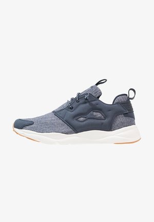 Zapatilla deportiva gris y negra con parte superior de tela, cierre de cordones, pestañas para tirar en la lengüeta y el talón, y suela blanca con suela exterior de goma.