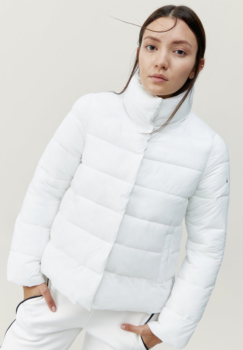 Chaqueta de plumas blanca con un cuello alto, que presenta secciones acolchadas y un bolsillo lateral. Acabado suave, diseño ligero.