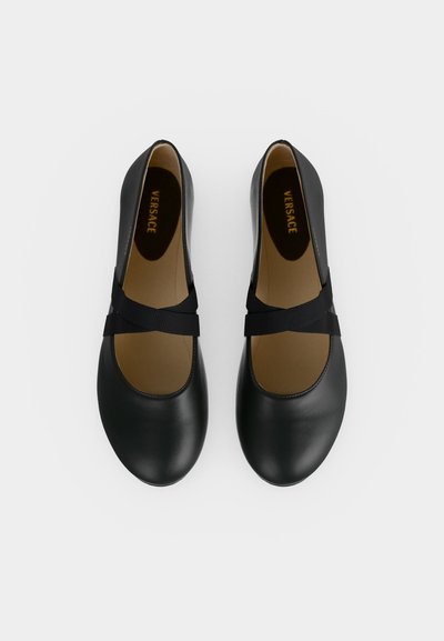 Paire de chaussures Mary Jane en cuir noir avec brides croisées en tissu noir et intérieur beige portant l'étiquette Versace.