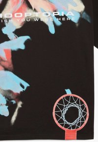 Sort stof t-shirt med farverige grafiske elementer, herunder abstrakte former i blå og pink samt et rødt basketballkurv design.