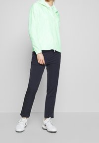 Light green, striped lightweight jacket with a hood, zipped front, paired with navy pants and white sneakers.