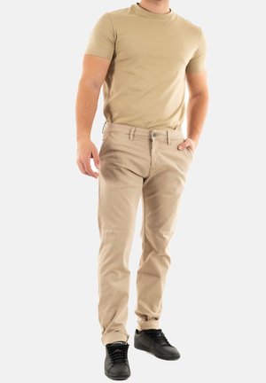 Pantaloni in cotone khaki con una vestibilità slim, abbinati a una t-shirt beige a maniche corte e sneakers nere, che conferiscono un'aspetto casual.