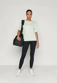 Svetlo zelena majica širokega kroja, črne legice, bele teniske in črna torba čez ramo. Enostaven dizajn, gladka tkanina, minimalističen stil.