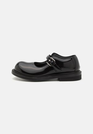 Black patent leather Mary Jane shoe with rounded toe, adjustable buckle strap, and flat sole. Smooth texture and minimalist design.