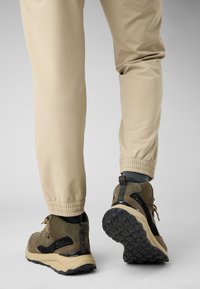 Beige tapered broek met elastische boorden en robuuste donkergroene en zwarte wandelschoenen, met gestructureerde materialen en duurzame zolen.