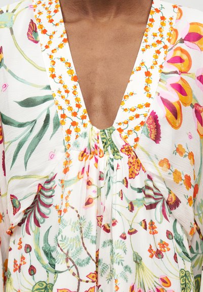 Φόρεμα με βαθιά V-λαιμόκοψη από λευκό ύφασμα με πολύχρωμα πορτοκαλί, ροζ και πράσινα λουλουδένια σχέδια και μικρό πορτοκαλί ανθάκι κατά μήκος της λαιμόκοψης.