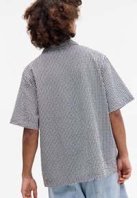 Camisa de manga curta em padrão de xadrez preto e branco, com colarinho e um corte descontraído. Feita de um tecido leve com uma textura suave.