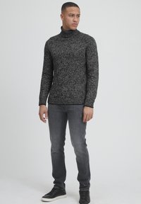 Gestreifter schwarzer und grauer Rollkragenpullover mit strukturiertem Muster, kombiniert mit enganliegenden grauen Jeans und schwarzen Turnschuhen.