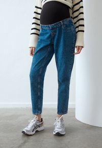 Ljusblå denimjeans med avslappnad passform, hög midja och uppvikta fållar, i kombination med vita och grå sportskor.