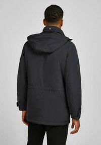 Veste isolée marine avec capuche, poignets élastiques et taille cintrée. Caractérisée par un accent logo subtil au dos et un matériau résistant à l'eau.