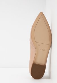 Escarpin en cuir beige à bout pointu, texture lisse, et talon bas marron solide avec logo sur la semelle.