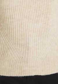Maglione a coste beige, caratterizzato da un motivo testurizzato con linee diagonali e una forma leggermente aderente. Materiale morbido e caldo.