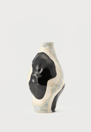 Abstrakte Keramikvase mit unregelmäßiger Form, die große schwarze, weiße und strukturierte blau-graue Flecken auf ihrer Oberfläche aufweist.