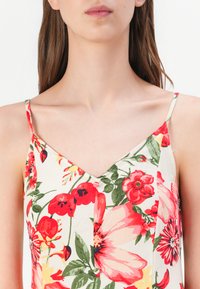 Top senza maniche con motivo floreale, caratterizzato da una scollatura a V, fiori rossi e rosa su uno sfondo crema, con spalline sottili.