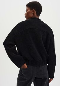Pullover nero oversize in maglia con tessuto testurizzato, spalle abbassate e orlo cropped. Indossato con jeans in denim scuri a vita alta.