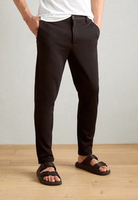 Pantaloni neri dal fit slim, con passanti per cintura e tasche anteriori abbinati a sandali neri con due cinturini regolabili. Tessuto morbido.
