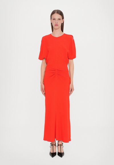 Rotes, knielanges Kleid mit kurzen Puffärmeln, das vorne Raffung aufweist und eine taillierte Silhouette hat, kombiniert mit schwarzen spitzen Absatzschuhen.