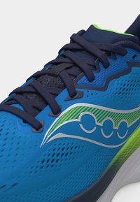 Μπλε αθλητικό παπούτσι με σκουρό μπλε κορδόνια, λογότυπα σε νέον πράσινο και ασημί χρώμα, ανθεκτικό δίχτυ στο πάνω μέρος και αναπαυτική σόλα.