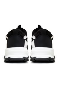 Scarpe da ginnastica in bianco e nero con una tomaia testurizzata e morbida, dettagli in pelle liscia e una suola intermedia bianca spessa e ammortizzata. Suola esterna in gomma nera.