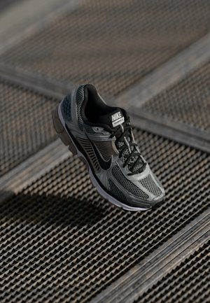 Der Nike Vomero 5 Sneaker verfügt über ein graues Mesh- und Synthetik-Obermaterial, schwarze Akzente, einen gepolsterten Kragen und eine dämpfende Sohle für zusätzlichen Komfort.