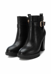 Botas negras de cuero hasta el tobillo con un tacón grueso, cremallera lateral y detalle de correa con hebilla. Textura suave con punta redondeada y suela con relieve.