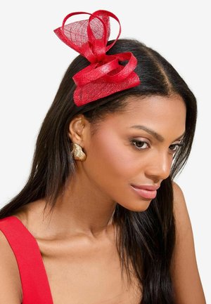 Punainen fascinator, jossa on kerroksellisia, läpikuultavia verkon nauhoja. Huipulla on suuri solmu ja teksturoitu, pyöreä pohja. Mukana kultasävytteiset korvakorut.