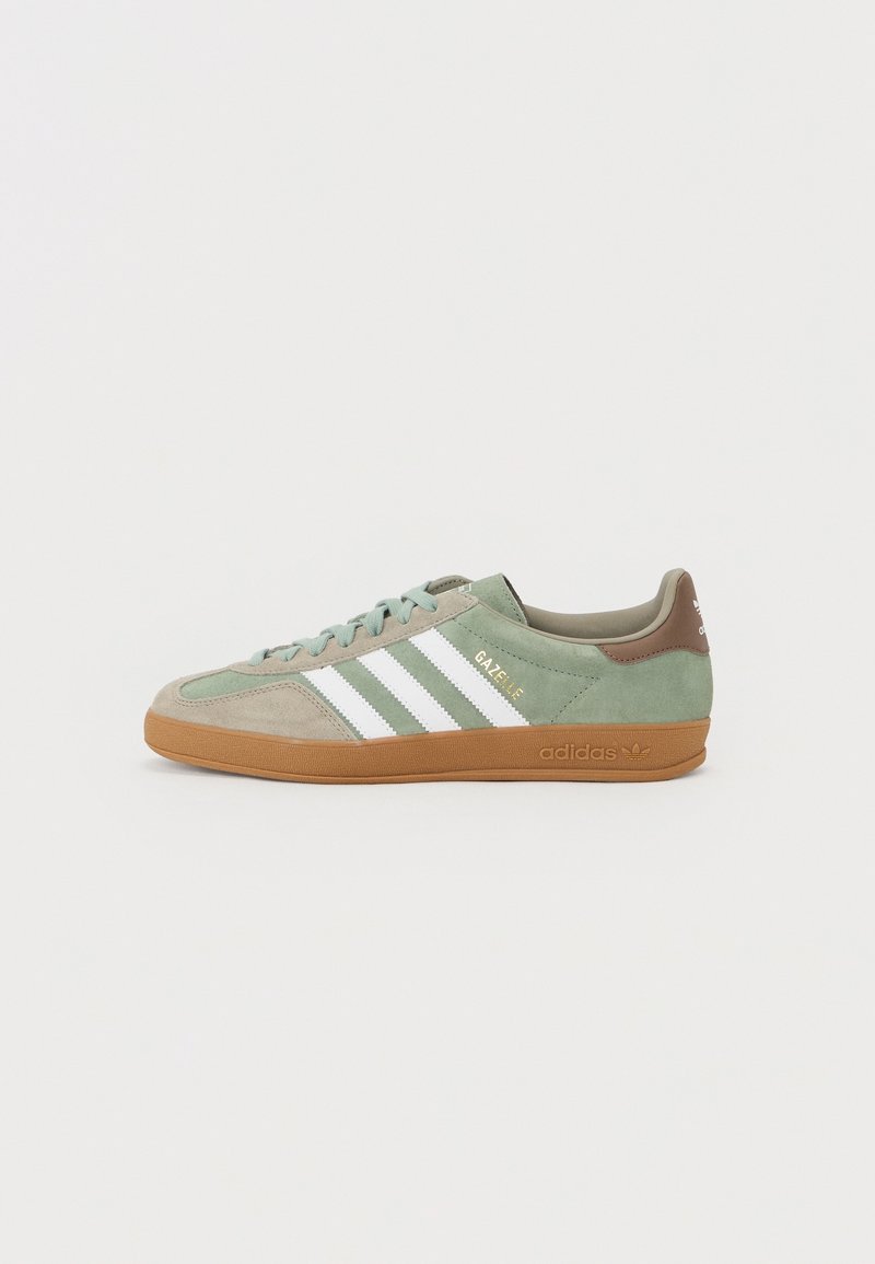 Groene en beige Adidas Gazelle sneaker met witte strepen en gumzool, zijaanzicht op een effen lichte achtergrond.