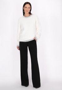Pulover alb, pufos, cu un guler și manșete texturate în dungi gri, asortat cu pantaloni largi, negri, cu talie înaltă.