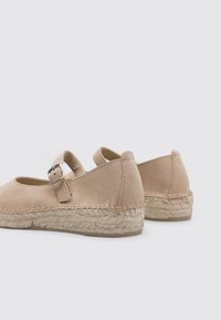 Espadrilles en suédine beige avec une bride au niveau de la cheville, bout rond et semelle en jute tressé. Caractéristiques : coutures minimales et texture lisse.