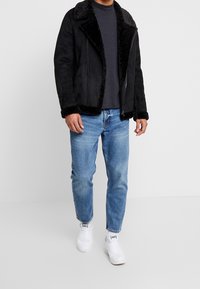 Musta keinoturkisnahkatakki pehmeällä mustalla turkiskauluksella ja -hihoilla, yhdistettynä tummanharmaaseen paitaan ja vaaleansinisiin farkkuihin. Valkoiset tennarit viimeistelevät asun.