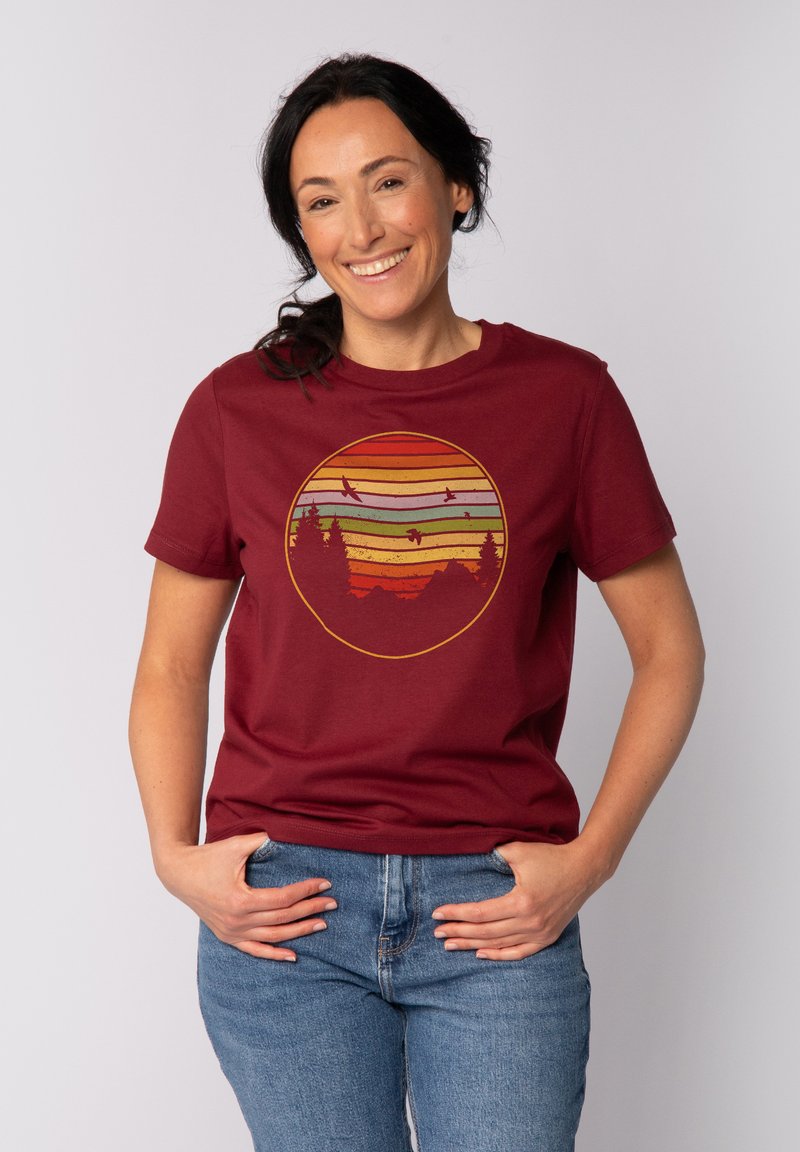 Bordeaux T-Shirt mit kurzen Ärmeln zeigt ein kreisförmiges Motiv eines Sonnenuntergangs mit geschichteten Farben sowie einer Silhouette von Bäumen und Vögeln.