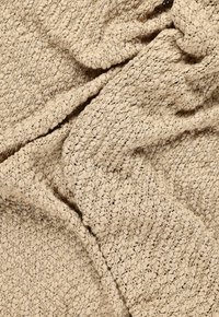 Beige leivottu viltti, jossa on tekstuuripinta, kohotetut silmukat ja hienovarainen kiilto, valmistettu pehmeästä materiaalista.