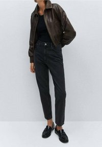 Chaqueta bomber de piel marrón, camiseta negra ajustada, jeans negros de cintura alta y mocasines negros. Texturas suaves y ajuste entallado.