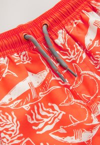 Shorts de bain orange vif avec un motif de requin blanc et de corail. Taille élastique avec cordons gris et détails en plastique.