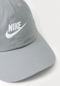 Γκρι μπέιζμπολ καπέλο κατασκευασμένο από υφαντό ύφασμα με κεντημένο λευκό λογότυπο "Nike" και σχέδιο Swoosh στο μπροστινό μέρος.