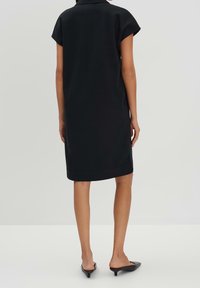 Czarna krótka sukienka z prostym krojem, kołnierzykiem i długością do kolan. Gładki materiał, minimalistyczne detale, zestawiona z czarnymi klapkami na obcasie.