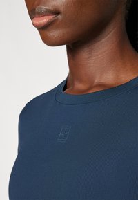 T-shirt a coste blu navy con scollatura rotonda e un sottile dettaglio del logo in rilievo sul petto. Tessuto liscio, design aderente.