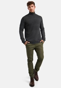 Maglione a collo alto lavorato a maglia di un grigio scuro con strisce testurizzate, abbinato a pantaloni verde oliva e stivali in cuoio marrone con lacci. Fit casual.
