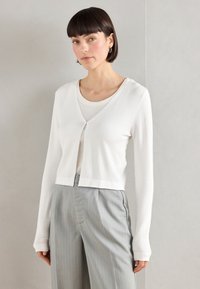 White long-sleeve cardigan with a V-neck and button closure, made of soft fabric; paired with a light gray striped wide-leg pant.