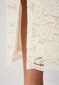 Jupe en dentelle crème, ornée d'un motif floral, avec des détails complexes à l'ourlet et une superposition en transparence révélant une doublure lisse.