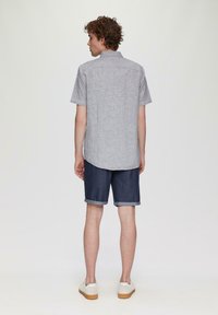 Grijs T-shirt met korte mouwen van een gestructureerde stof, gecombineerd met donkerblauwe denim shorts. Witte sneakers maken de outfit compleet.