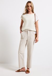 Lys beige bomulds t-shirt med blonde detaljer, parret med lys beige højtaljede bukser med forlommer. Brune snørebåndssandaler.